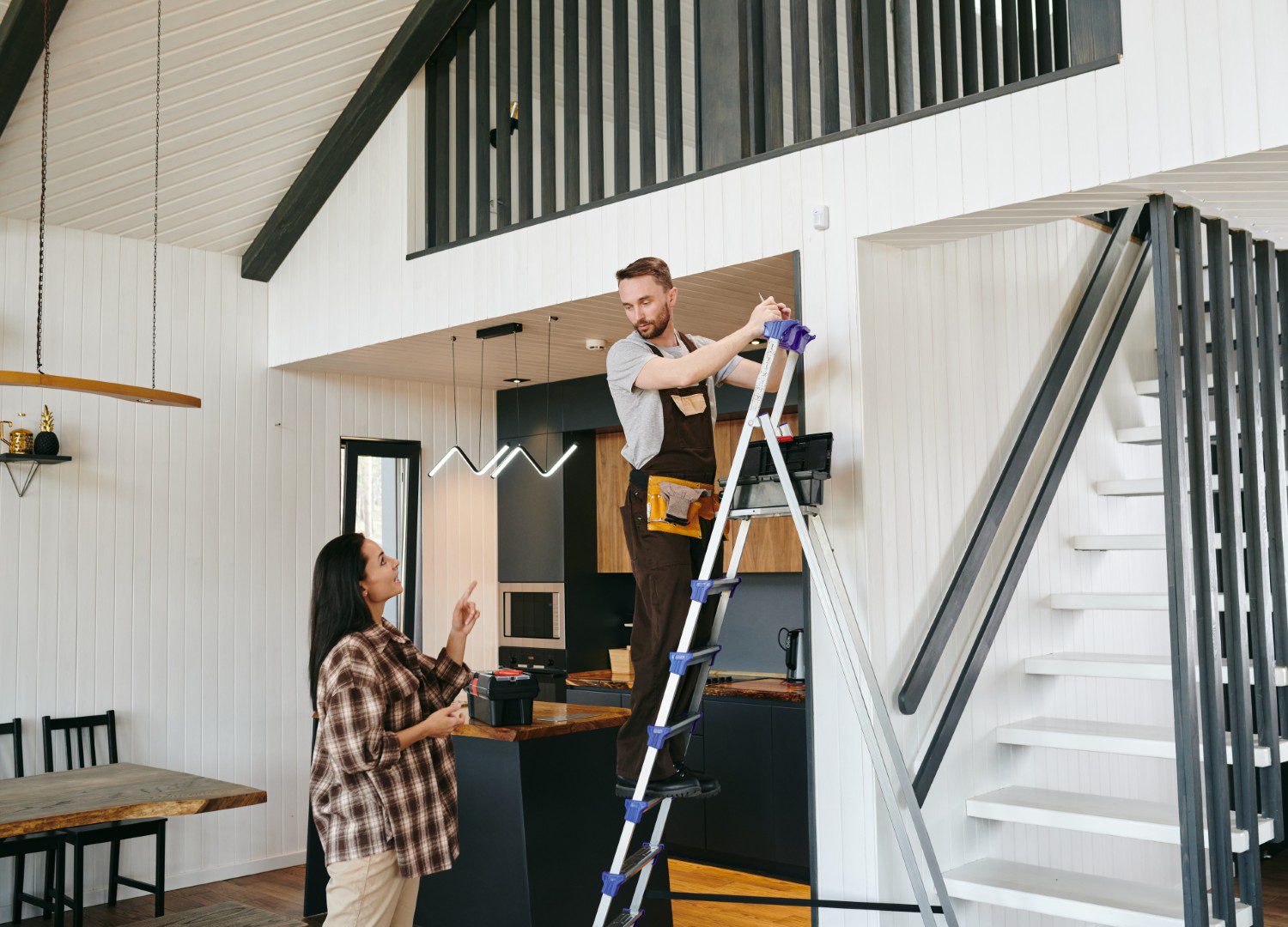 Man on ladder working, woman watching nearby.