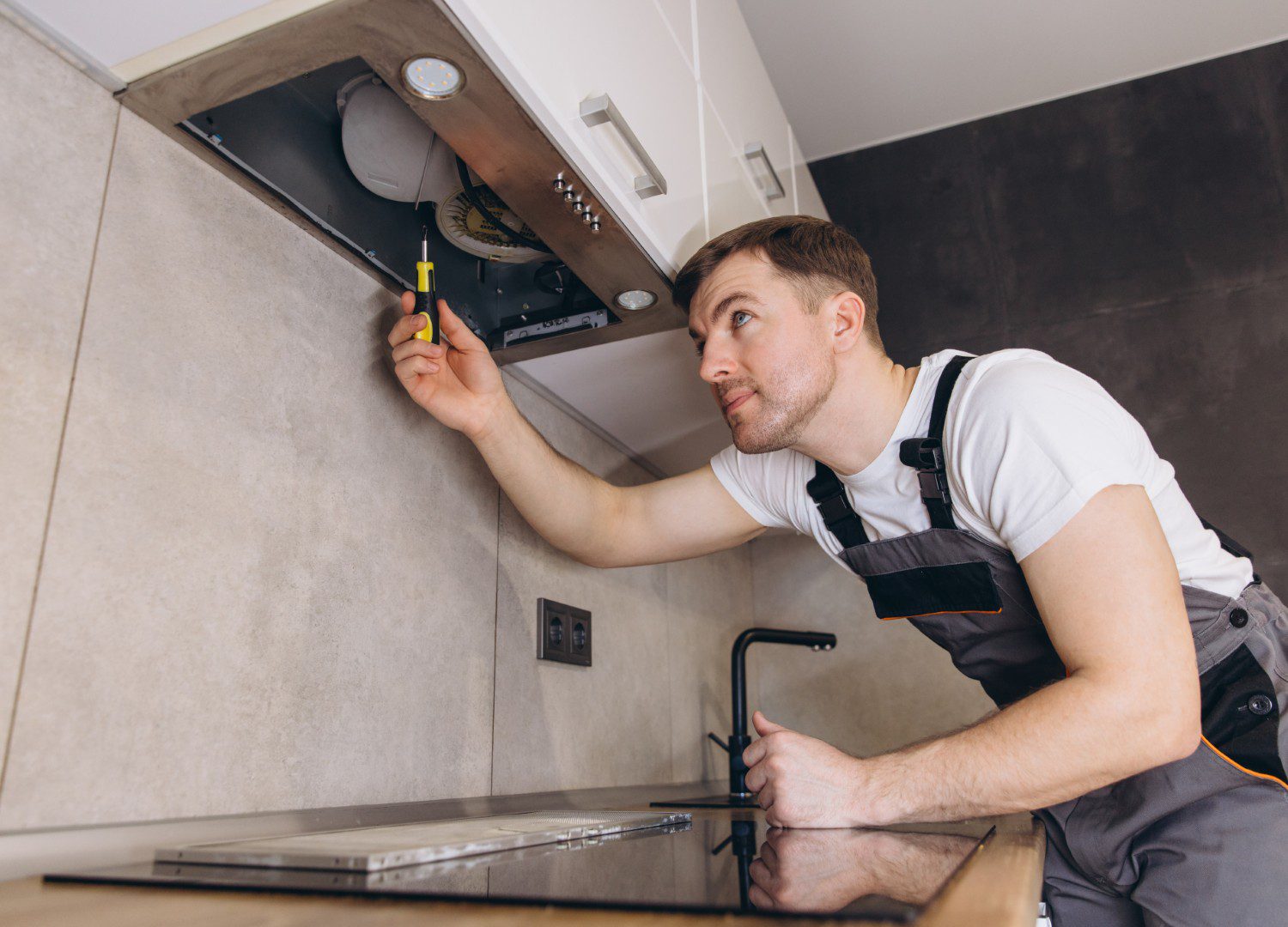 Man repairing kitchen extractor hood with screwdriver.